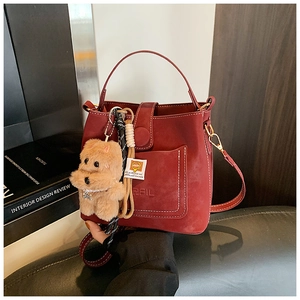 Detail of dark red matte bucket bag with white stitching and plush dog charm