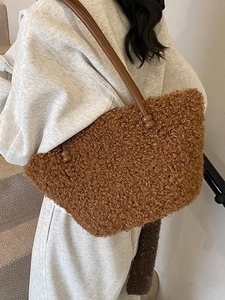 Brown fuzzy plush bucket bag with leather strap worn by a model on a gray background