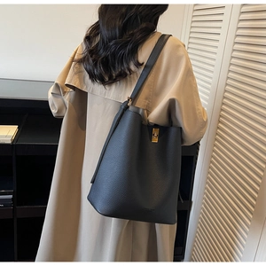 Détail du sac seau noir en cuir grainé avec fermoir doré sur un manteau beige