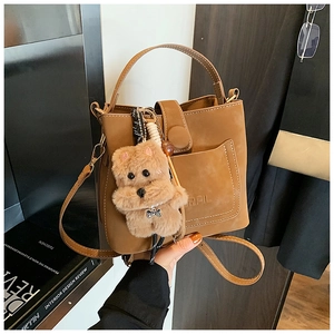 Close-up of retro brown bucket bag with plush bear charm and adjustable shoulder strap