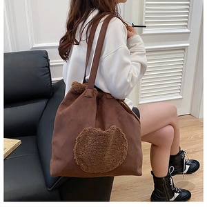 Detail of a brown suede tote bag with a dark brown plush heart patch and drawstring close