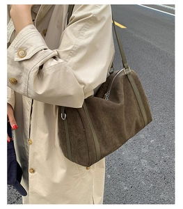 Détail du sac Boston en daim marron avec bandoulière verte porté sur un trench-coat beige