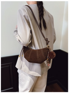 Detail of dark brown suede crescent bag with knot strap and stylish pompom charm accessory