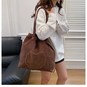 Detail view of large brown suede tote with dark brown fuzzy heart patch and drawstring design