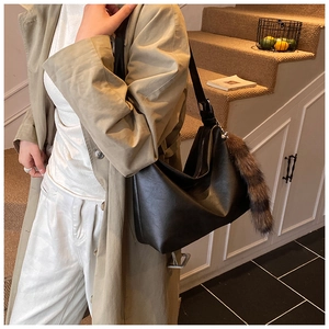 Detail of black faux leather hobo bag with striped faux fox tail charm and adjustable strap