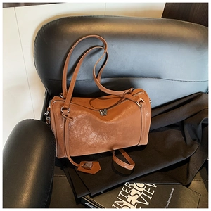 Detailed close-up of brown vintage texture barrel bag with metal lock charm on a leather chair