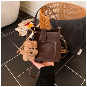Detail view of brown textured bucket bag with MERFIL logo and cute dog plush charm