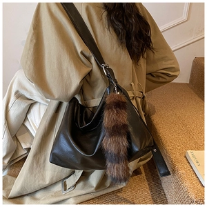 Close-up of black oversized tote bag with a striped plush charm on a khaki trench coat