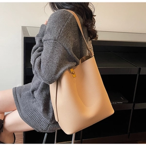 Détail du sac seau en cuir beige avec fermoir rotatif en métal doré et texture grainée