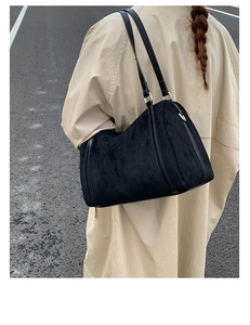 Détail du sac Boston en daim noir porté avec un trench-coat beige en extérieur