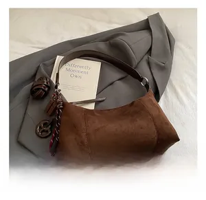 Détail du sac baguette en daim marron avec corde tressée colorée et ornements suspendus
