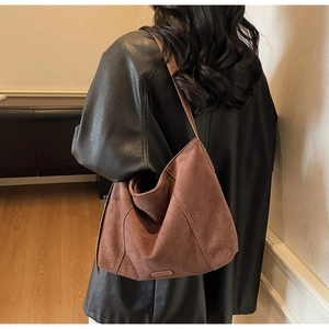 Detail of a dark brown suede tote bag featuring contrast stitching and a side strap design