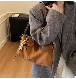 Détail d'un sac bandoulière en daim marron avec pompons en perles et plaque logo métal