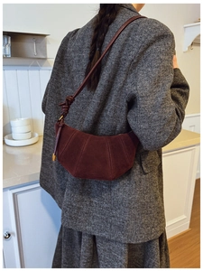 Detail of burgundy suede croissant bag showing premium stitching on a tweed coat