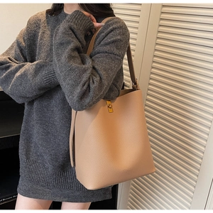Vue détaillée d'un sac seau en cuir grainé beige avec fermoir doré porté par un mannequin