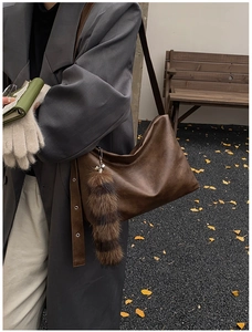 Brown retro leather tote bag with fluffy charm detail on a classic autumn street background