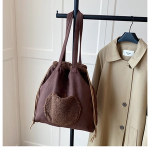 Detail of a brown suede tote bag with a plush heart pocket and drawstring closure