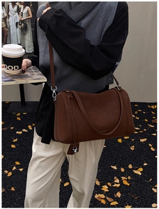 Close-up of matte dark coffee Boston bag with adjustable strap and metal lock pendant