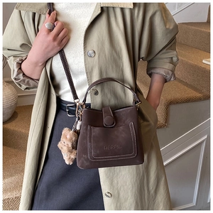 Detail of dark brown matte leather crossbody bag with teddy bear charm and top handle