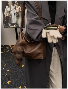 Detail of vintage brown leather hobo bag with striped plush charm in autumn setting