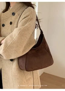 Détail du sac hobo en daim marron foncé avec coutures verticales sur un manteau beige