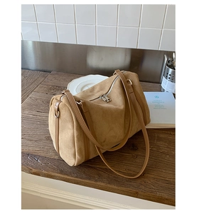 Détail du sac boston en daim kaki avec lanières en cuir marron sur une table en bois