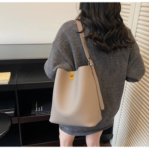 Détail du sac seau en cuir taupe avec fermoir pivotant doré porté par un mannequin