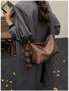 Detail of a large dark brown hobo bag with a faux fur tail charm and ginkgo leaves