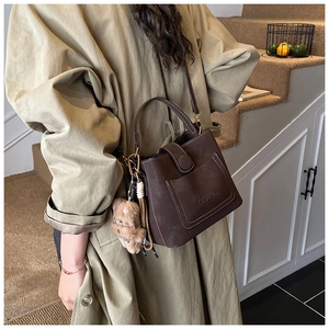 Detail of dark brown vintage bucket bag with contrast stitching and a plush bear charm
