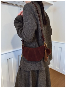 Detail of dark brown suede crescent bag with crossbody strap and decorative tassel accents