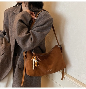 Détail du sac hobo en daim marron avec breloques en perles de bois et plaque logo
