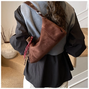 Détail du sac en daim marron avec bandoulière en cuir et accessoire tressé coloré