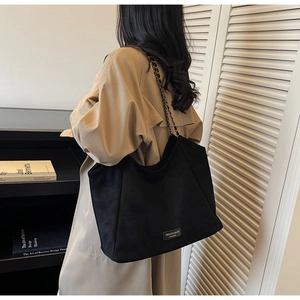 Détail d'un grand cabas en daim noir avec bandoulière chaîne et étiquette mode sur le devant