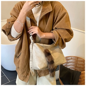 Detail view of beige tote bag featuring a fluffy faux fur tail charm and wide shoulder strap
