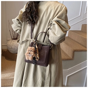Detail of dark brown leather crossbody bag with white stitching and puppy charm