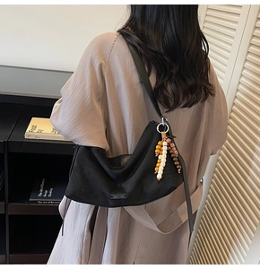 Détail du sac à bandoulière noir mat minimaliste avec charm perlé et étiquette en tissu