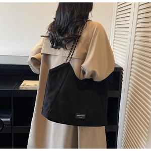 Détail du sac cabas en daim noir avec bandoulière chaîne et plaque métallique de marque