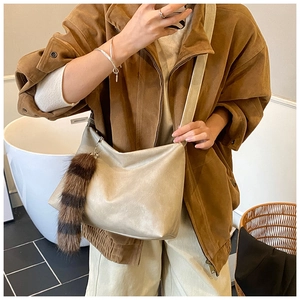 Close-up of beige hobo bag with striped faux fur tail charm and soft leather texture