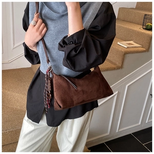 Détail d'un sac en daim marron avec un pompon tissé élégant sur la bandoulière