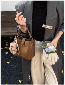 Brown leather bucket bag with white stitching detail and a cute plush bear charm