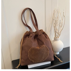 Close-up of brown suede bucket bag featuring a plush heart patch and drawstring closure