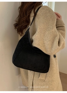 Détail d'un sac hobo en daim noir avec coutures verticales sur un manteau de laine beige