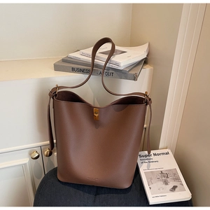 Détail du sac seau en cuir marron foncé avec fermoir rotatif en métal et texture grainée