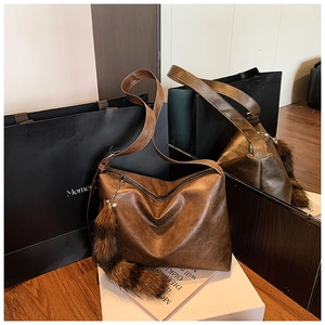 Detail view of vintage brown leather hobo bag with zipper and decorative fur tail charm