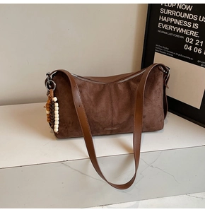 Détail du sac bandoulière en daim mat avec breloque en perles de bois et plaque logo métal