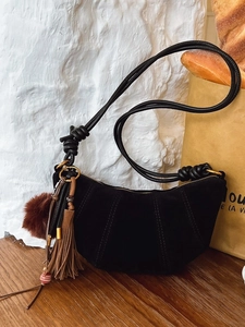 Retro black nubuck crescent bag with fringes and plush ball on a wooden table