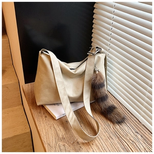 Detail of beige hobo shoulder bag with a unique striped plush tail charm on a wooden desk