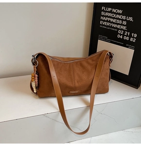 Détail du sac à bandoulière en daim marron avec plaque logo et breloque en perles colorées