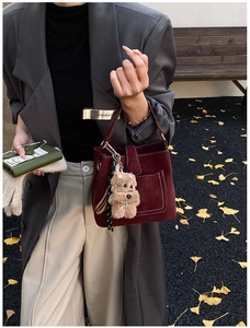 Detail of burgundy bucket bag with contrast stitching and teddy bear charm accessory