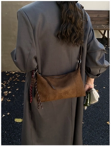 Détail du sac polochon en daim marron avec pendentif tressé sur un manteau d'hiver gris